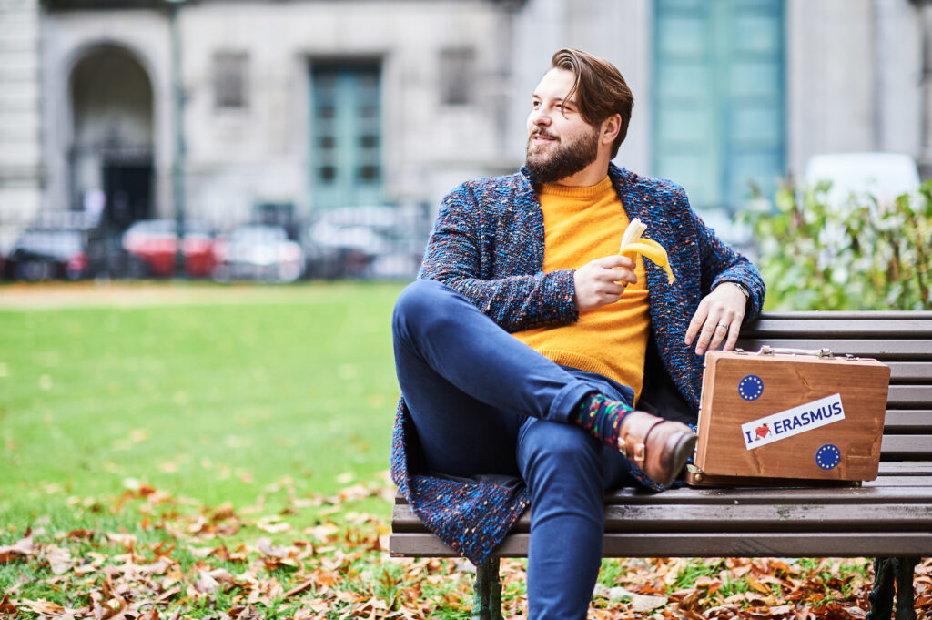 Young man on bench with EU Erasmus suitcase